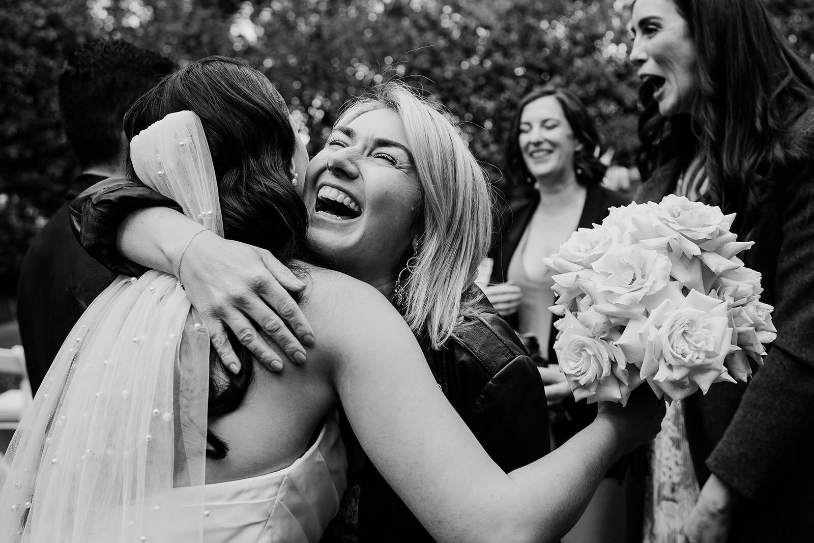 Black and white: a bride laughing as she hugs a friend among her bridesmaids