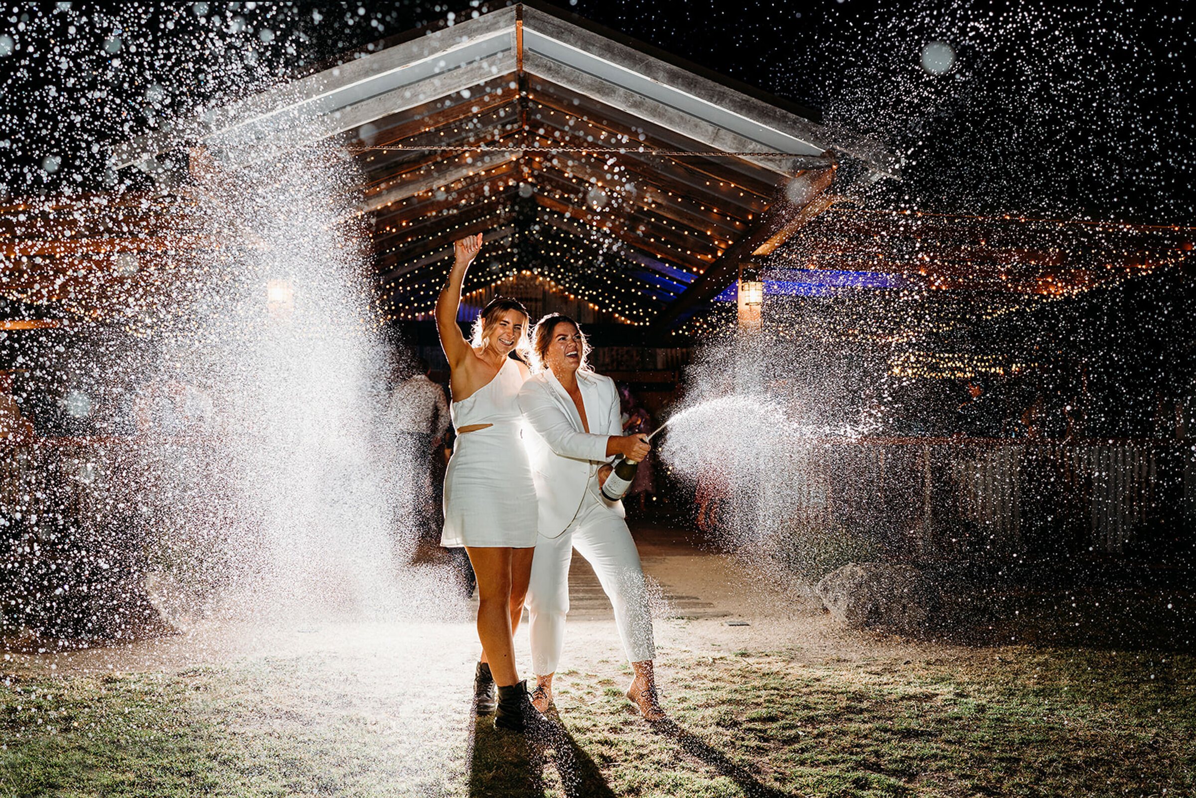 Two brides kissing at night in the rain under a spray of sparks