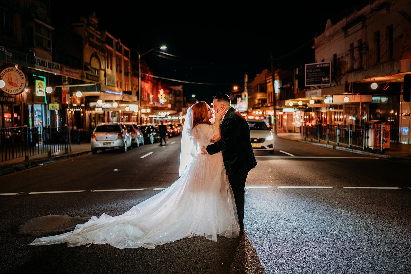 A couple kissing in the middle of a lit-up Newtown street at night