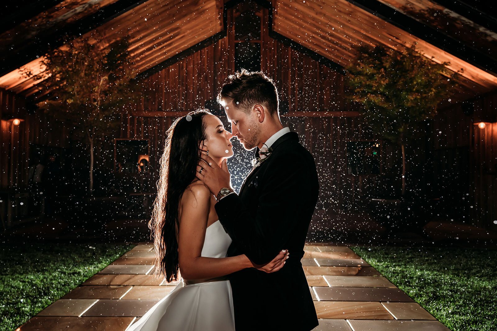 A couple kissing at night under a lit timber pavilion