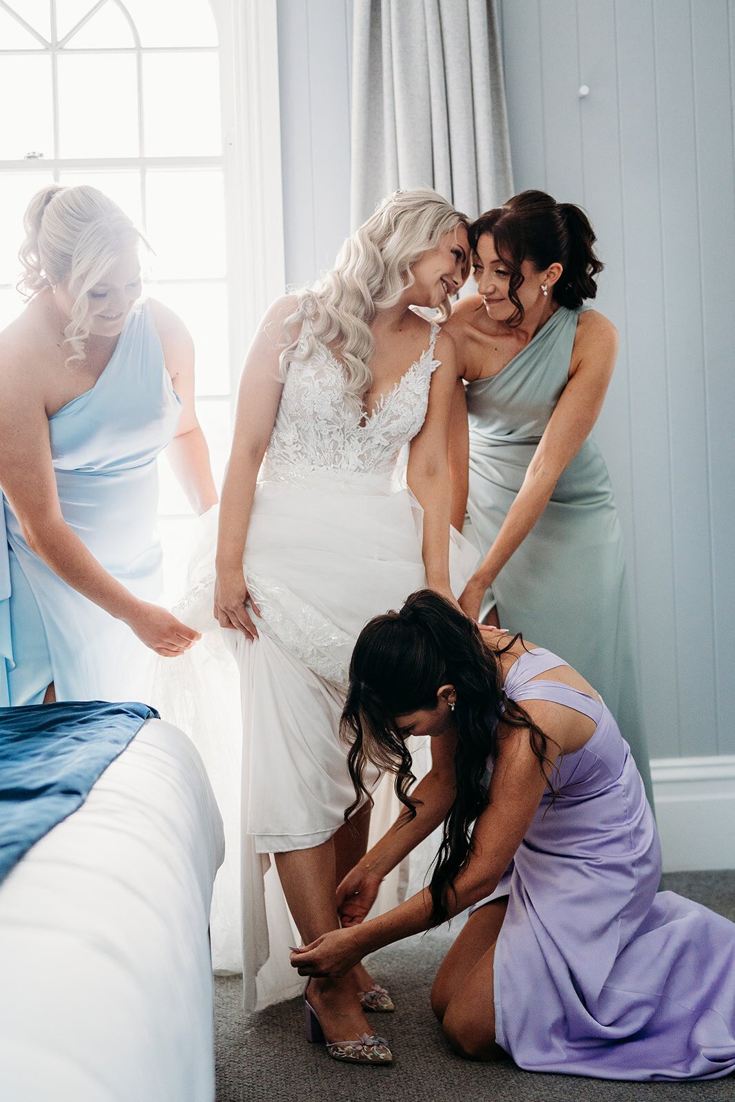 Bridesmaids fussing over a bride as one kneels to fasten her shoe